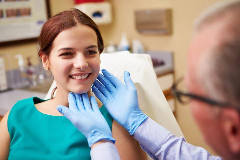 A beautiful girl is smiling while a dentist is examining her teeth