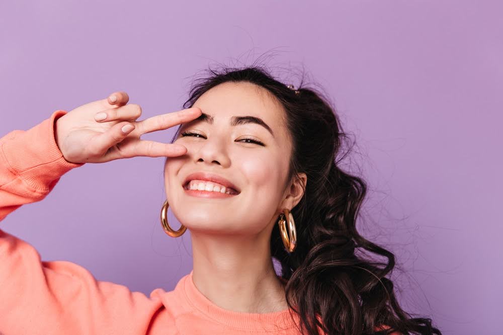 A stunning Asian female model showing a peace sign and a laughing camera