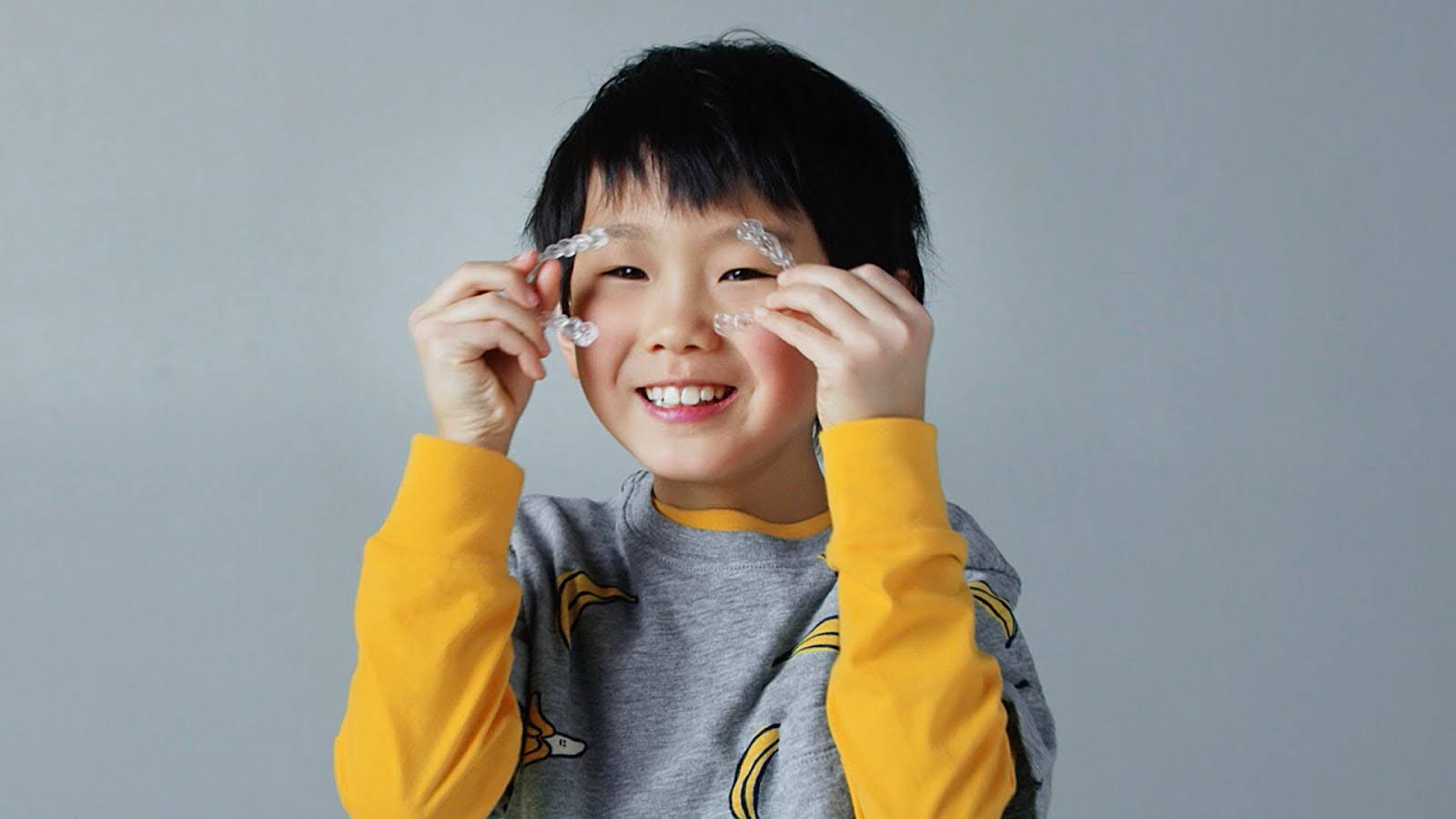  A young boy holding up his invisalign aligners