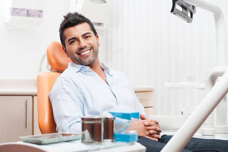  A happy, smiling male sitting on the dental chair at the dentist's office waiting for ozone treatment near him for his teeth.