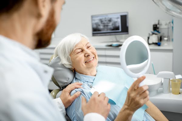 A woman looking at her teeth in a mirror, happy she decided to use oral sedation dentistry A woman looking at her teeth in a mirror, happy she decided to use oral sedation dentistry