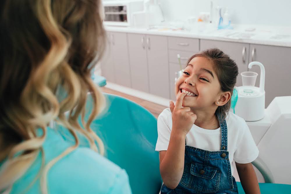  A young girl pointing to her teeth in a dentist's chair