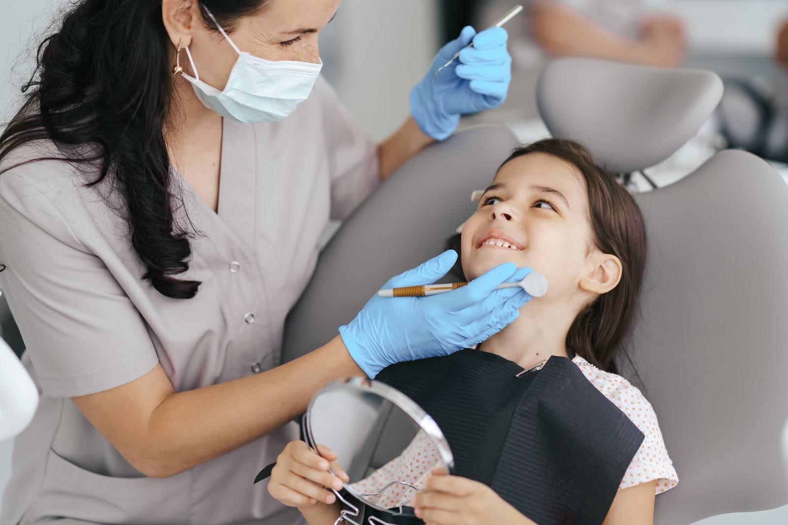  A young girl in a dentist chair with a dentist getting ready to do a check-up