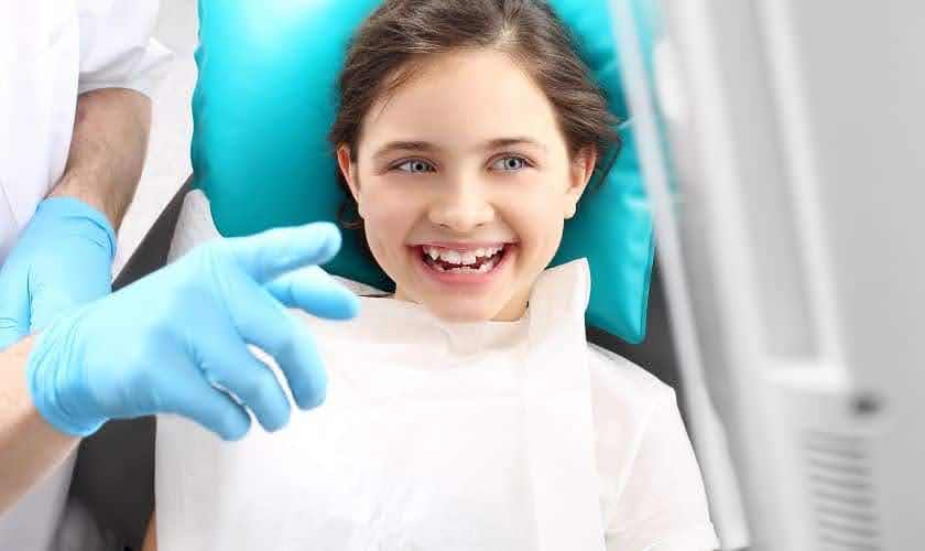  A young smiling girl looking where a dentist is pointing
