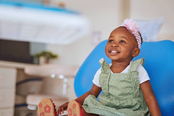  A happy young girl in a green dress sits in a dental chair, smiling brightly during her visit.