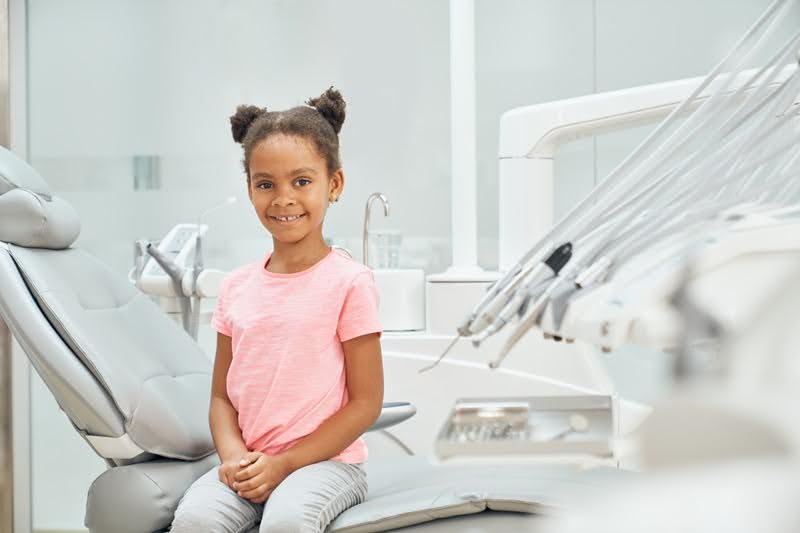   A beautiful little girl smiling and sitting on a dental chair.