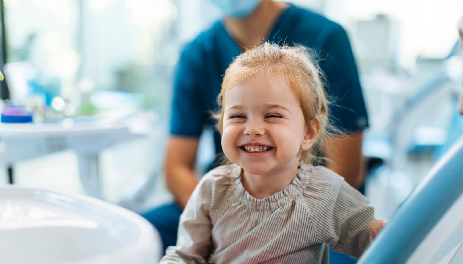   An adorable, cute little girl smiling while sitting at a kid's dental office specializing in preventive dentistry.