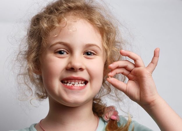  A young girl happily holding up her tooth that has just been extracted