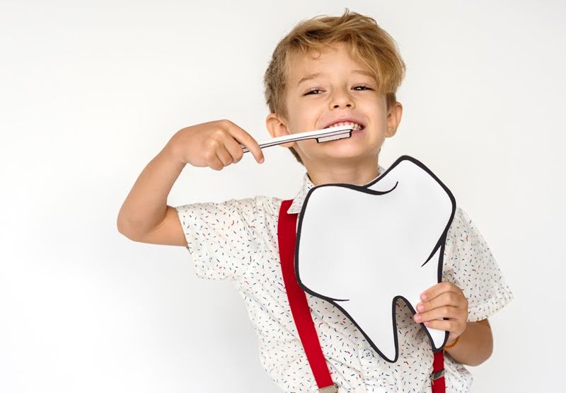  An adorable kid holding a brush and a paper tooth cut out, waiting for his pediatric stainless steel crown placement