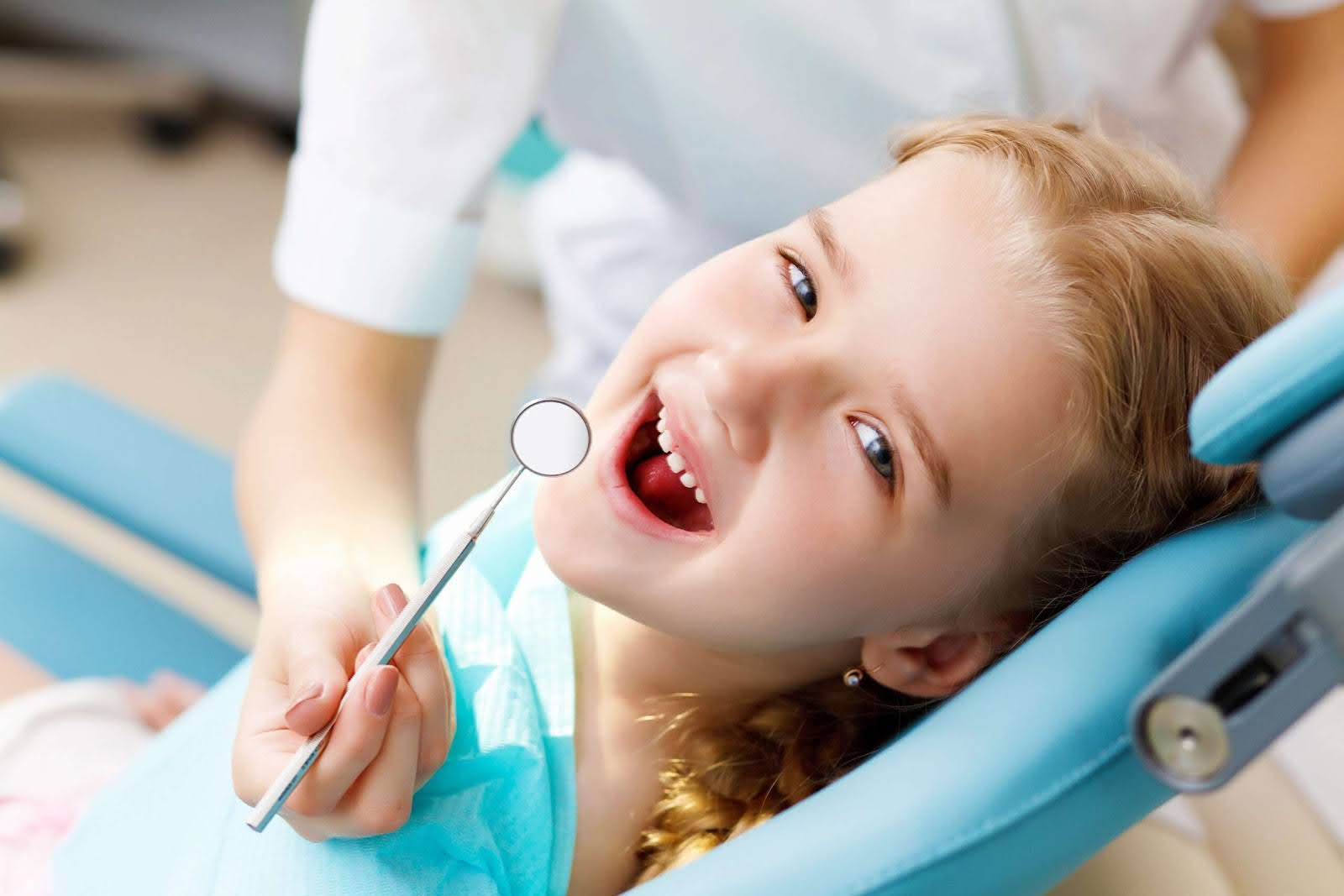   A smiling young girl at the dentist's office opens her mouth for a children's cavity dental checkup.